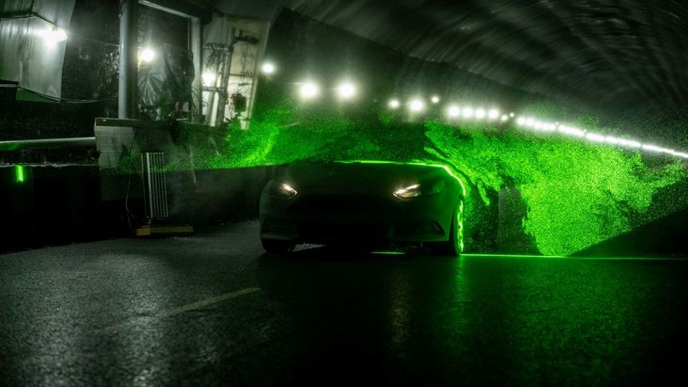A car drives through a sheet of helium-filled soap bubbles illuminated with a laser