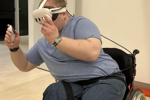 Wheelchair user wearing VR googles holding a controller leaning to avoid hazards in the VR game, Beat Saber
