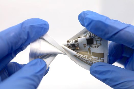 Pictured is a stretchable wearable devices incorporated on a newly developed material substrate that can adjust its dielectric properties to counter the disruptive effects of motion on interfacing electronics. The performance of the system was tested under various types of deforming motions, including twisting